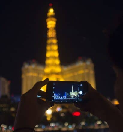 Foto de silhueta de pessoa tirando uma foto com o celular da Torre Eiffel de Las Vegas, iluminada ao fundo na parte da noite.