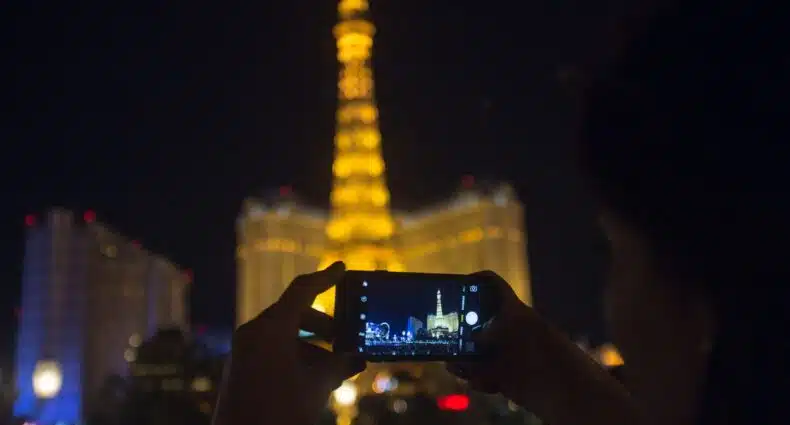 Foto de silhueta de pessoa tirando uma foto com o celular da Torre Eiffel de Las Vegas, iluminada ao fundo na parte da noite.