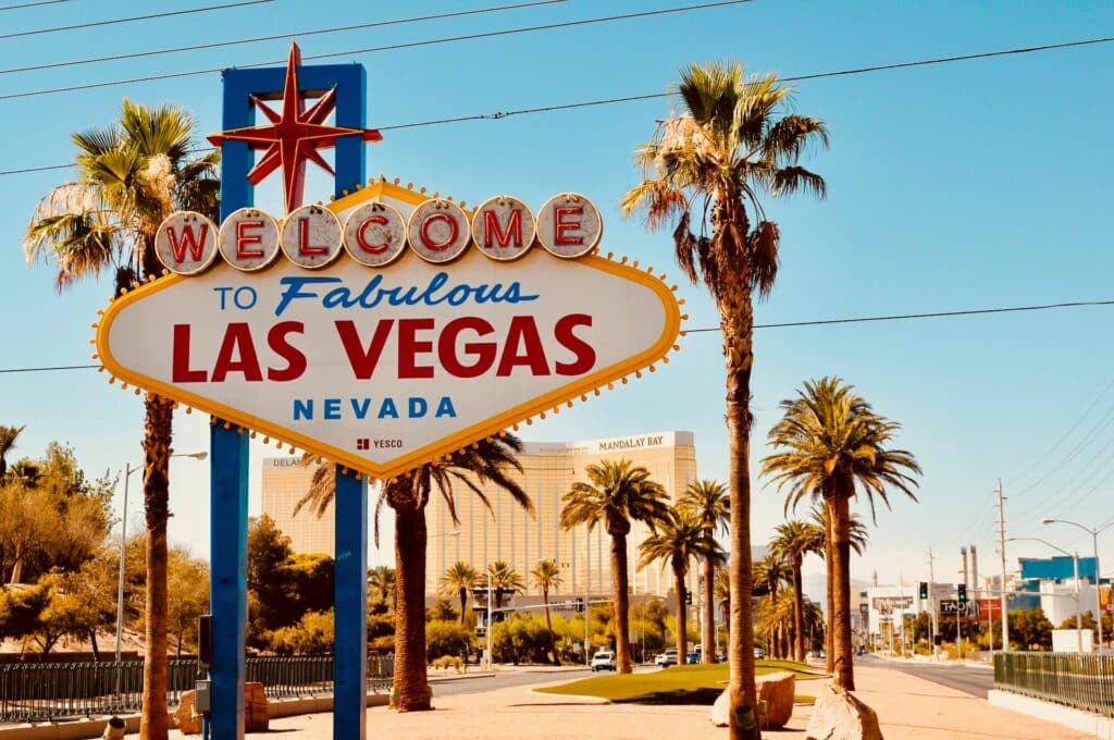 Placa de boas-vindas à Las Vegas na entrada da cidade, com palmeiras ao entrono, uma estrada ao lado, e hotel ao fundo para representar o chip de celular Las Vegas.