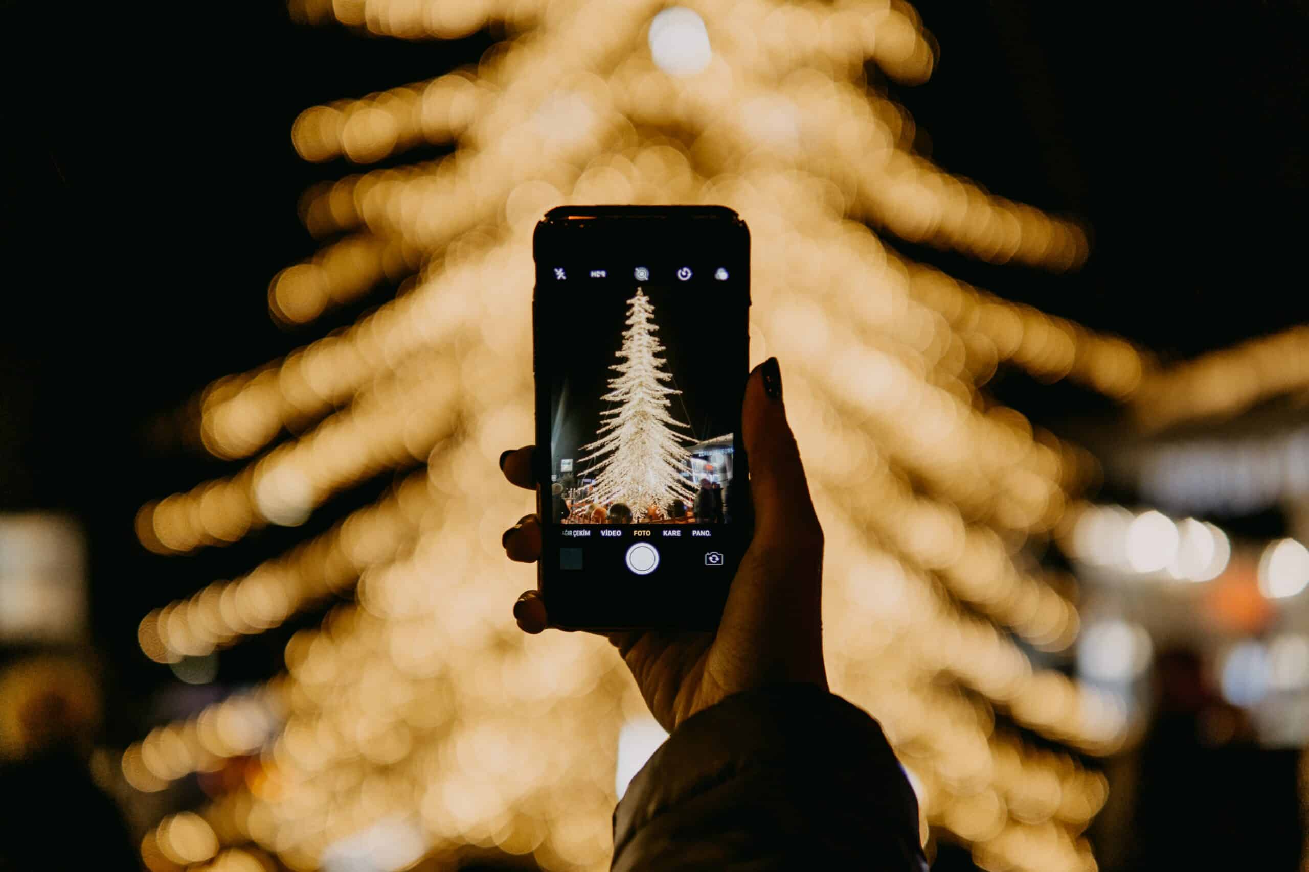 Celular na mão para tirar foto de árvore de natal iluminada a noite. Representa chip de celular Turquia