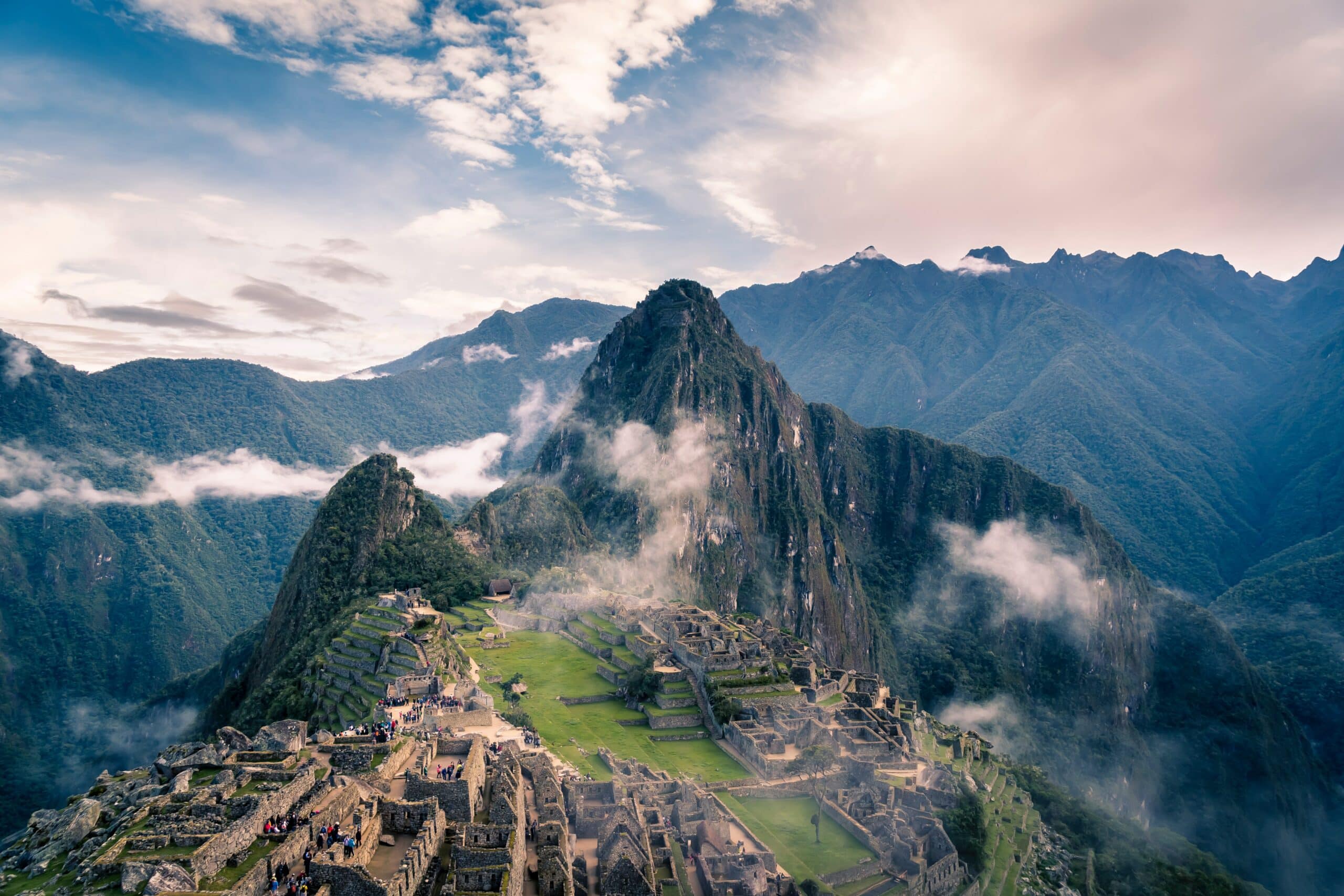 Vista de cima de Machu Picchu em meio as ruínas, no alto das montanhas com nuvens.