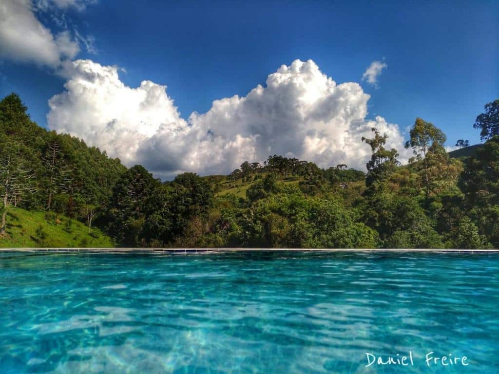 Piscina de borda infinita em um dia ensolarado com água azul e vista para montanhas e natureza verde da Serra da Mantiqueira