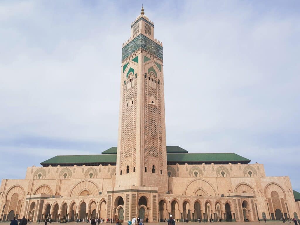 vista da frente da Mesquita Hassan II, com seu minarete muito alto e ricamente decorado em tons de azul como todo o restante da estrutura, com muitos arabescos, para ilustrar o post de chip celular Casablanca