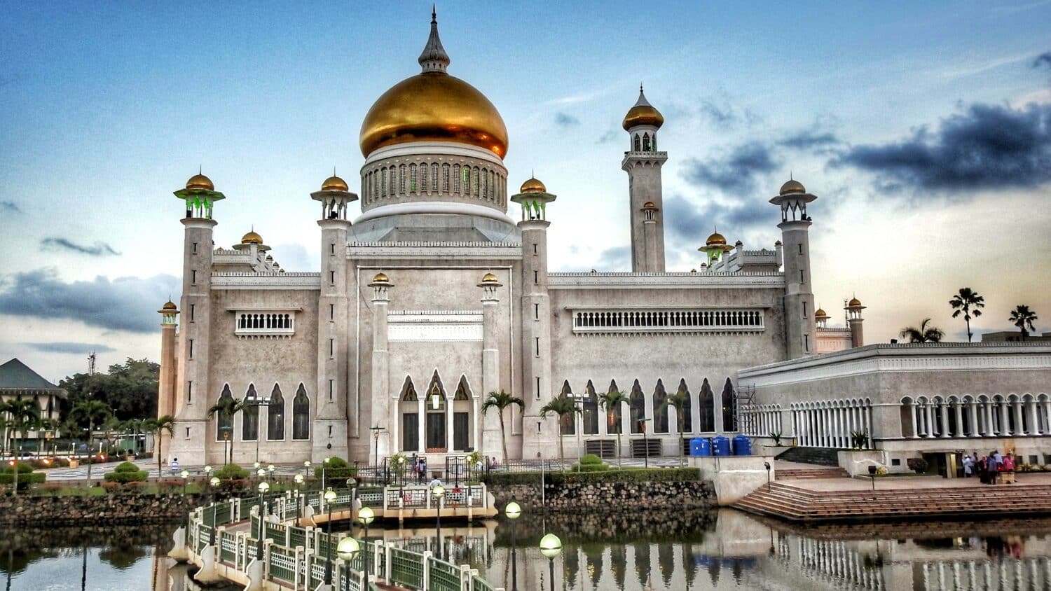 Vista da Grande Mesquita de Omar Ali Saifuddin, Brunei de cor branca, teto dourado, com várias janelas em frente ao lago durante o dia. Representa chip celular Brunei