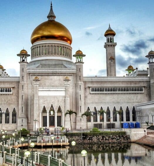 Vista da Grande Mesquita de Omar Ali Saifuddin, Brunei de cor branca, teto dourado, com várias janelas em frente ao lago durante o dia. Representa chip celular Brunei