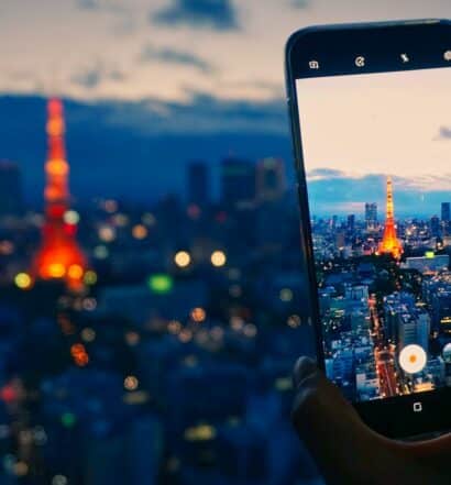 Um celular sendo usado para fotografar a cidade de Tóqui com foco na Torre de Tóquio, que se parece um pouco com a Torre Eiffel