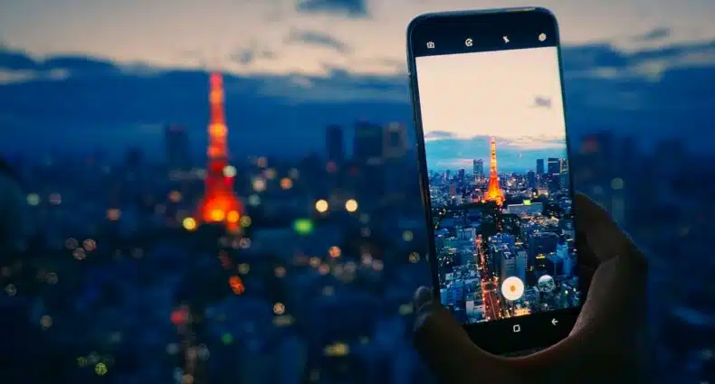 Um celular sendo usado para fotografar a cidade de Tóqui com foco na Torre de Tóquio, que se parece um pouco com a Torre Eiffel