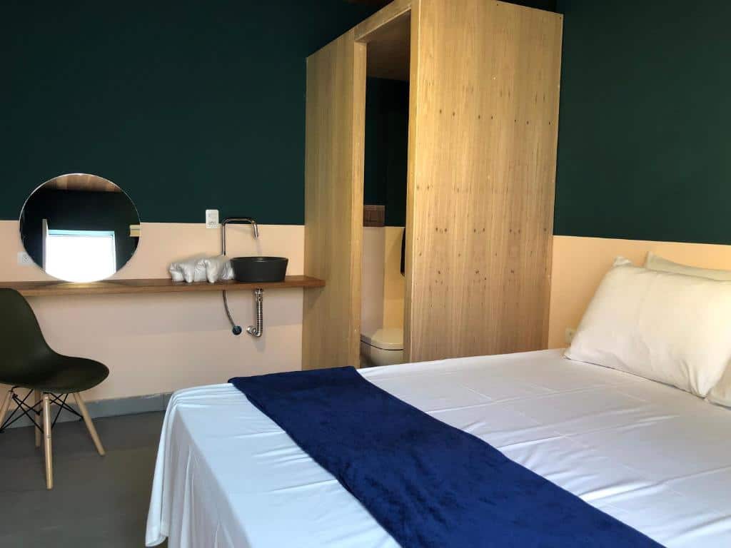 Quarto do Ô de Casa Hostel com uma cama de casal, uma bancada com um espelho, uma pequena cuba e toalhas, e pequeno lavabo