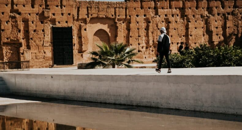 homem andando em uma passarela que leva até as ruínas de pedra em tons de terra e areia do Palácio El Badi, em Marrakesh, para ilustrar o post de chip celular Marrocos