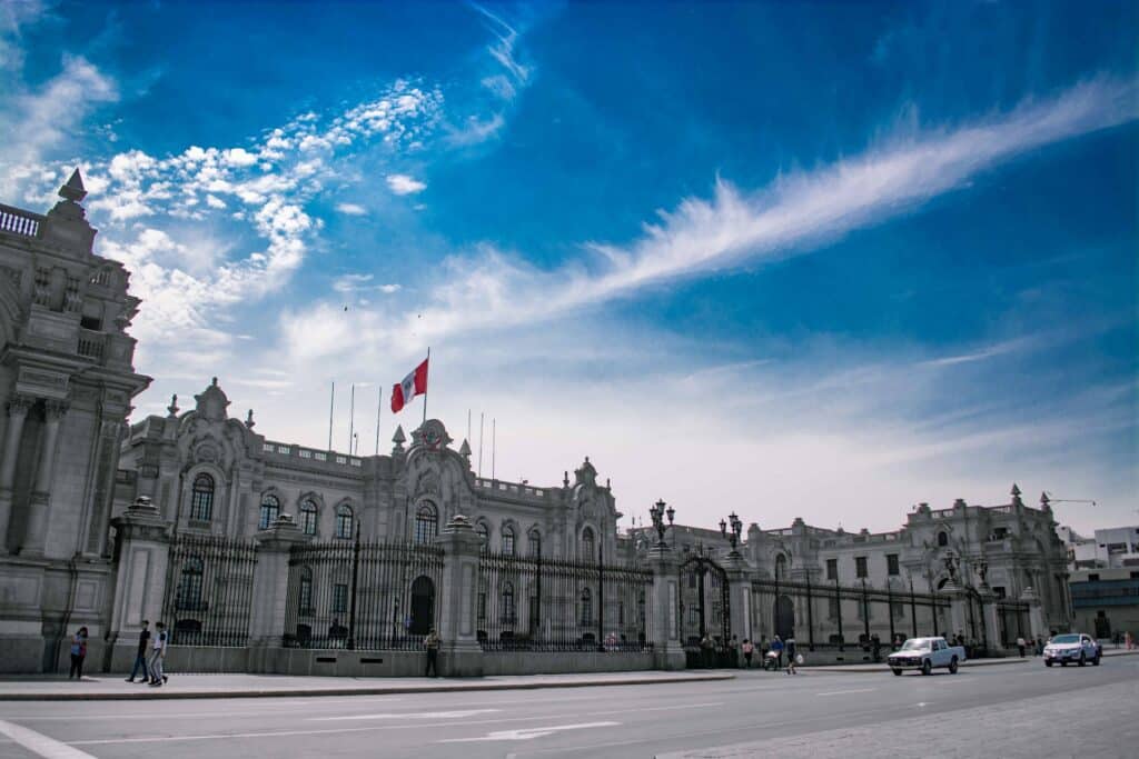 vista do Palácio do Governo do Peru, em Lima, sendo uma construção cinza clássica, com diversas janelinhas e uma bandeira do país acima
