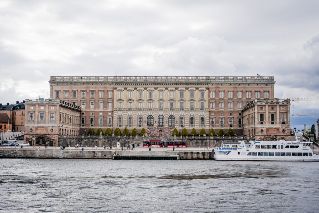 fachada do Palácio Real de Estocolmo com estrutura clássica europeia em tons de ocre com um rio na frente