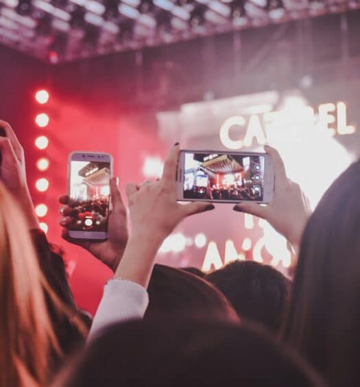 Pessoas tirando foto de um show durante a noite. Há luzes vermelhas refletindo no fundo da imagem. - Foto: Noralí Nayla via Unsplash