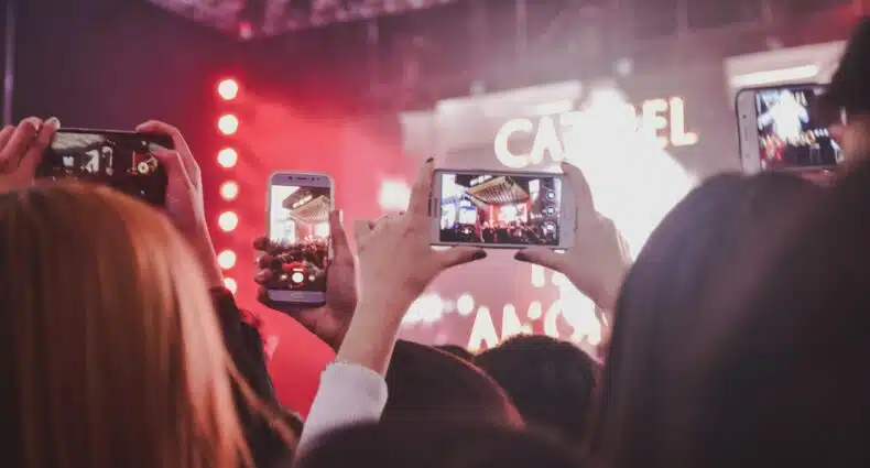 Pessoas tirando foto de um show durante a noite. Há luzes vermelhas refletindo no fundo da imagem. - Foto: Noralí Nayla via Unsplash