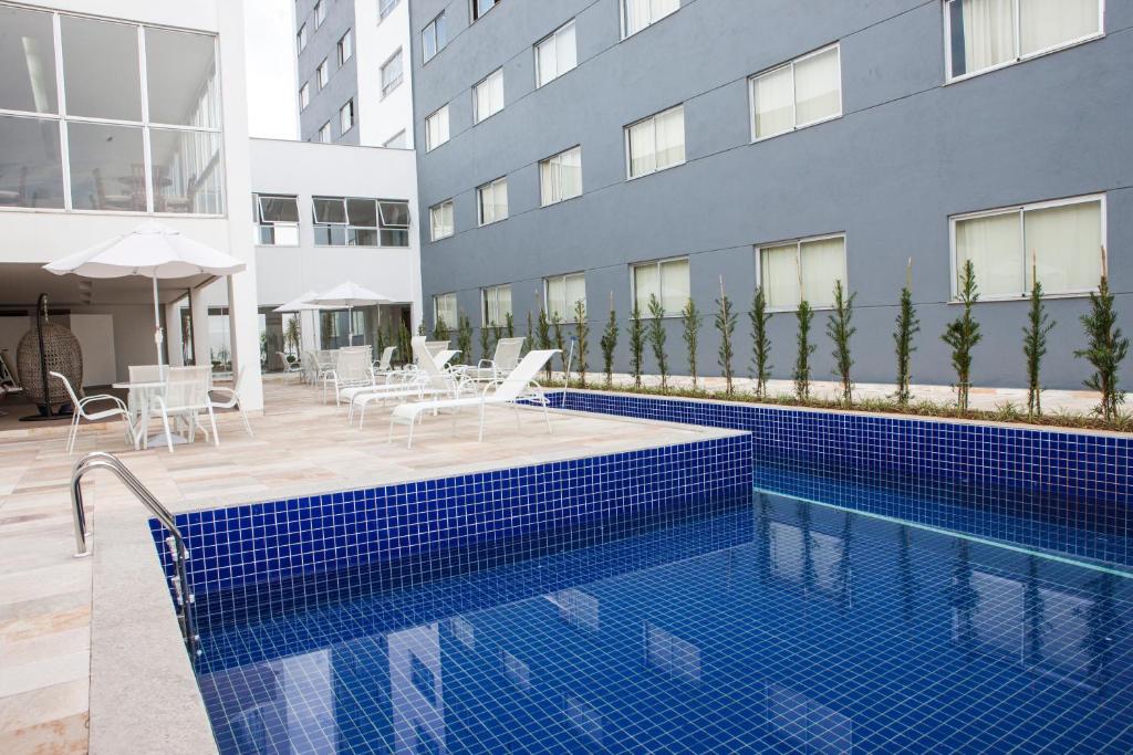 piscina retangular com escada e área externa com espreguiçadeiras brancas e uma varanda com acesso ao Hotel Abba Uno, em Betim, a fachada é cinza clara e tem várias janelinhas
