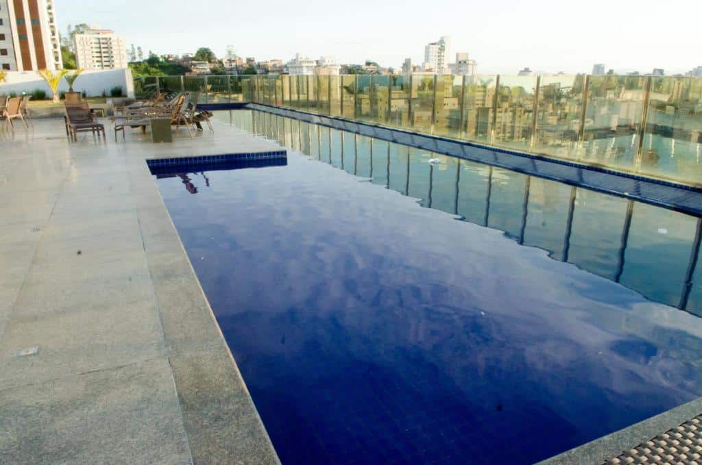 Vista da piscina do Ville Celestine Condo Hotel, na cobertura do hotel com vista para a cidade e cadeiras com mesas ao fundo. Representa hotéis em Belo Horizonte