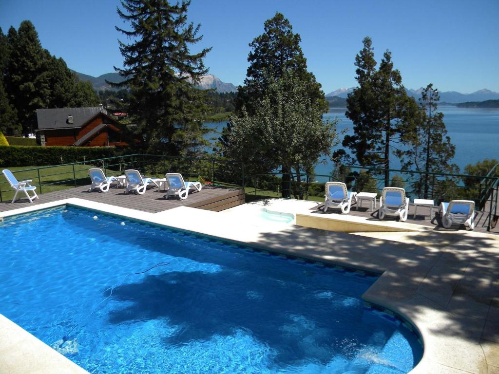 Vista da piscina do Charming Luxury Lodge & Private Spa durante ao dia com cadeiras perto da piscina e ao fundo vista para o mar. Representa hotéis em Bariloche