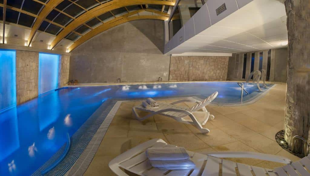 Piscina coberta do Hotel Cristal com cadeiras perto da borda da piscina. Representa hotéis em Bariloche