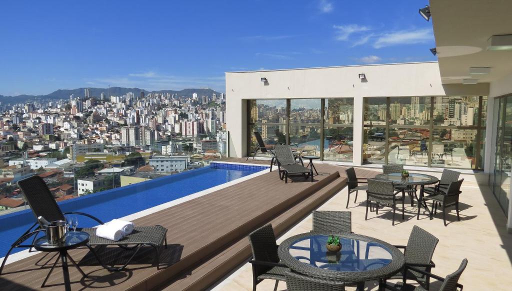Vista da piscina do Hotel Beaga Convention Expominas by MHB na cobertura do prédio com cadeiras e mesa em volta, com vista para a cidade durante o dia. Representa hotéis em Belo Horizonte.