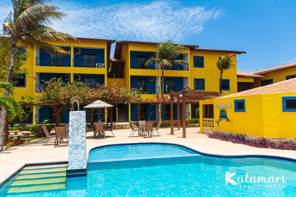 Vista da piscina do Kalamari Beach Hotel  com cadeiras em frente ao edifício amarelo. Representa hotéis perto do Beach Park