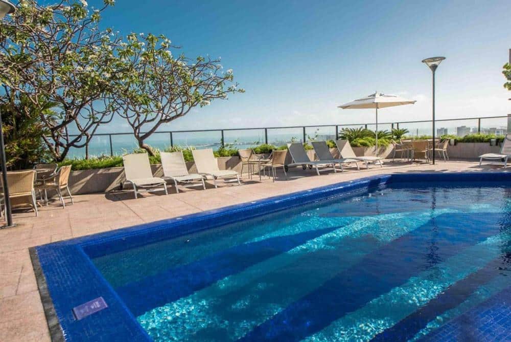 Vista de dia da piscina do Hotel Gran Marquise com cadeiras em volta em frente ao mar.