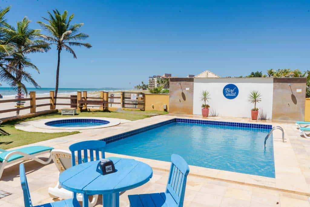 Vista da piscina do Milos Beach Hotel com cadeira e mesa azul de madeira do em frente e a piscina atrás. Representa hotéis perto do Beach Park