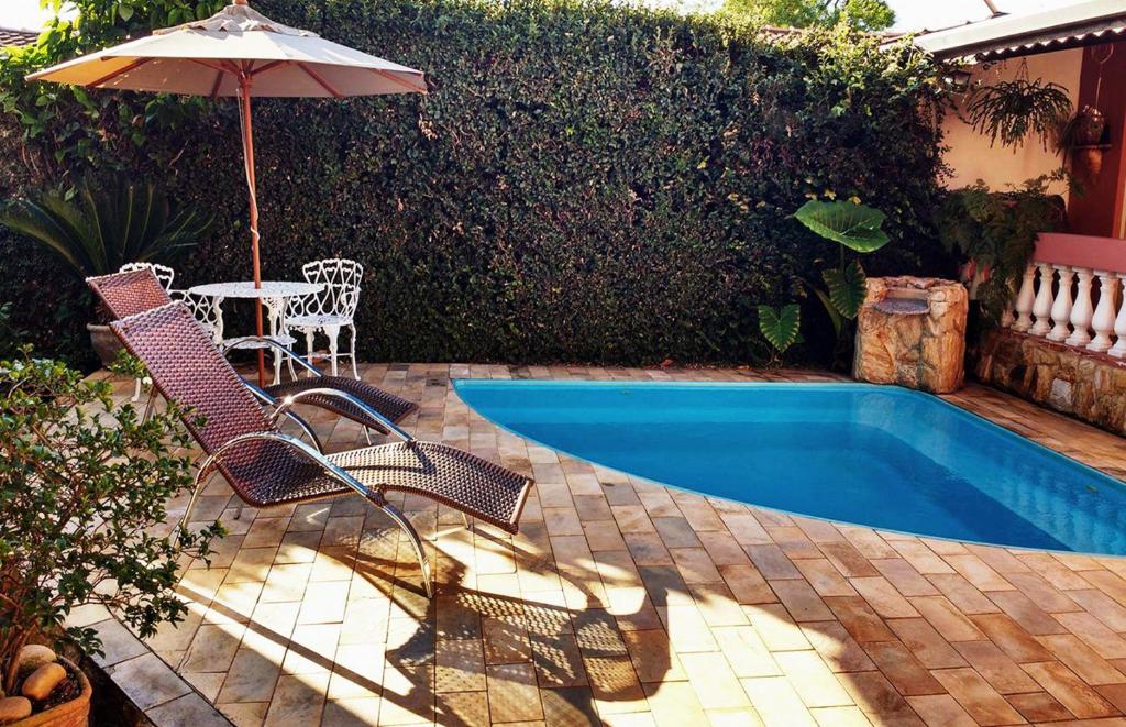 Vista da piscina da Piccola Pousada com cadeiras perto da borda em dia de sol. Representa pousadas em Águas de São Pedro