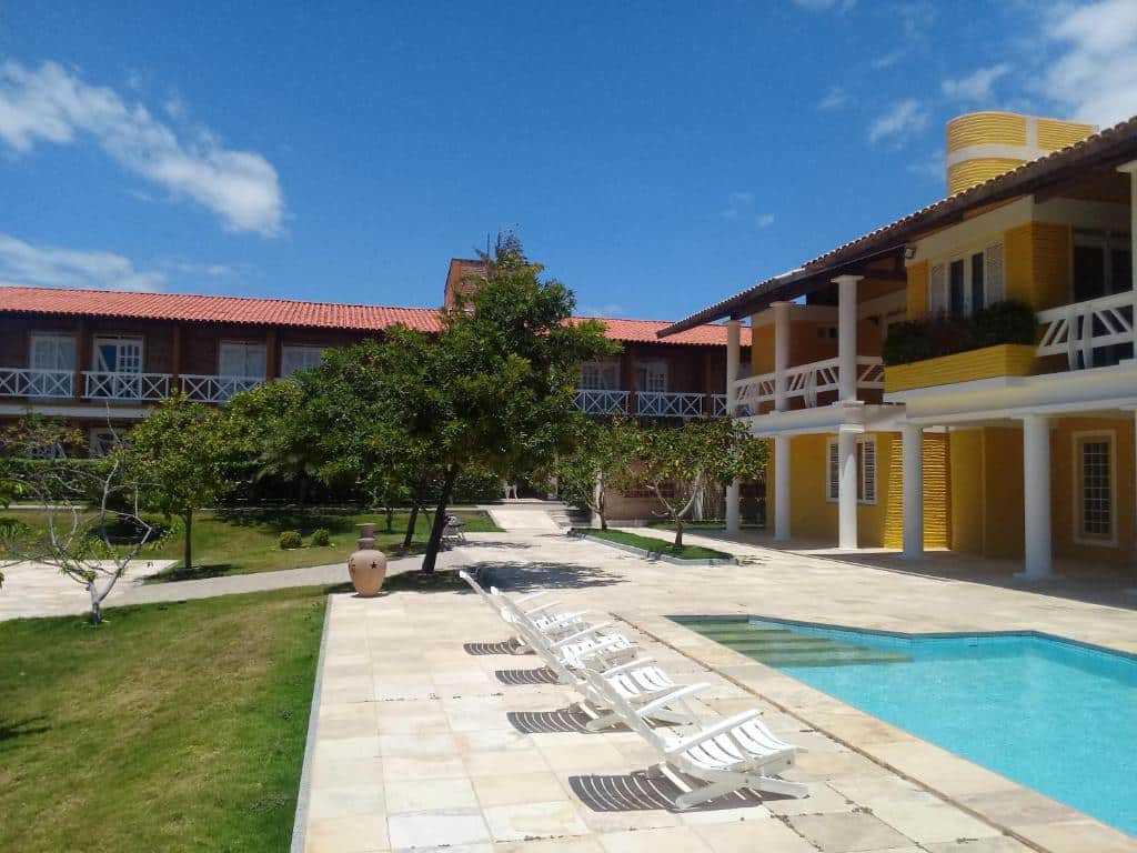 Vista da piscina do Hotel Porto Belo em dia de sol com cadeiras perto da piscina e atrás o hotel de cor amarela. Representa hotéis perto do Beach Park
