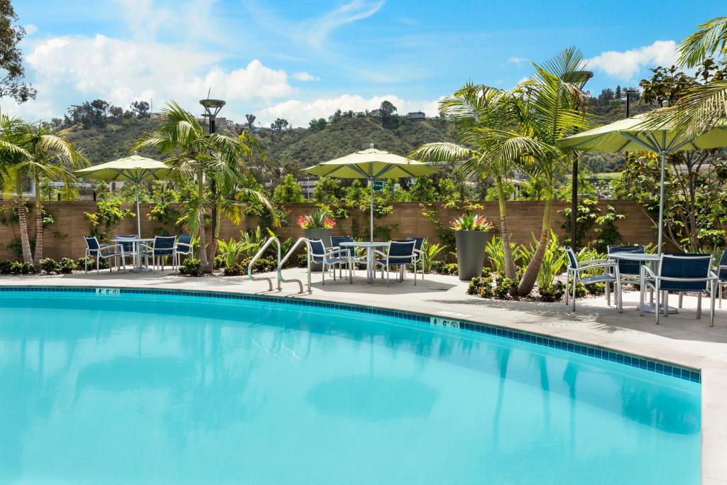 Vista da piscina do SpringHill Suites by Marriott San Diego Mission Valley com cadeiras na beira da piscina com guarda-sóis. Representa hotéis em San Diego