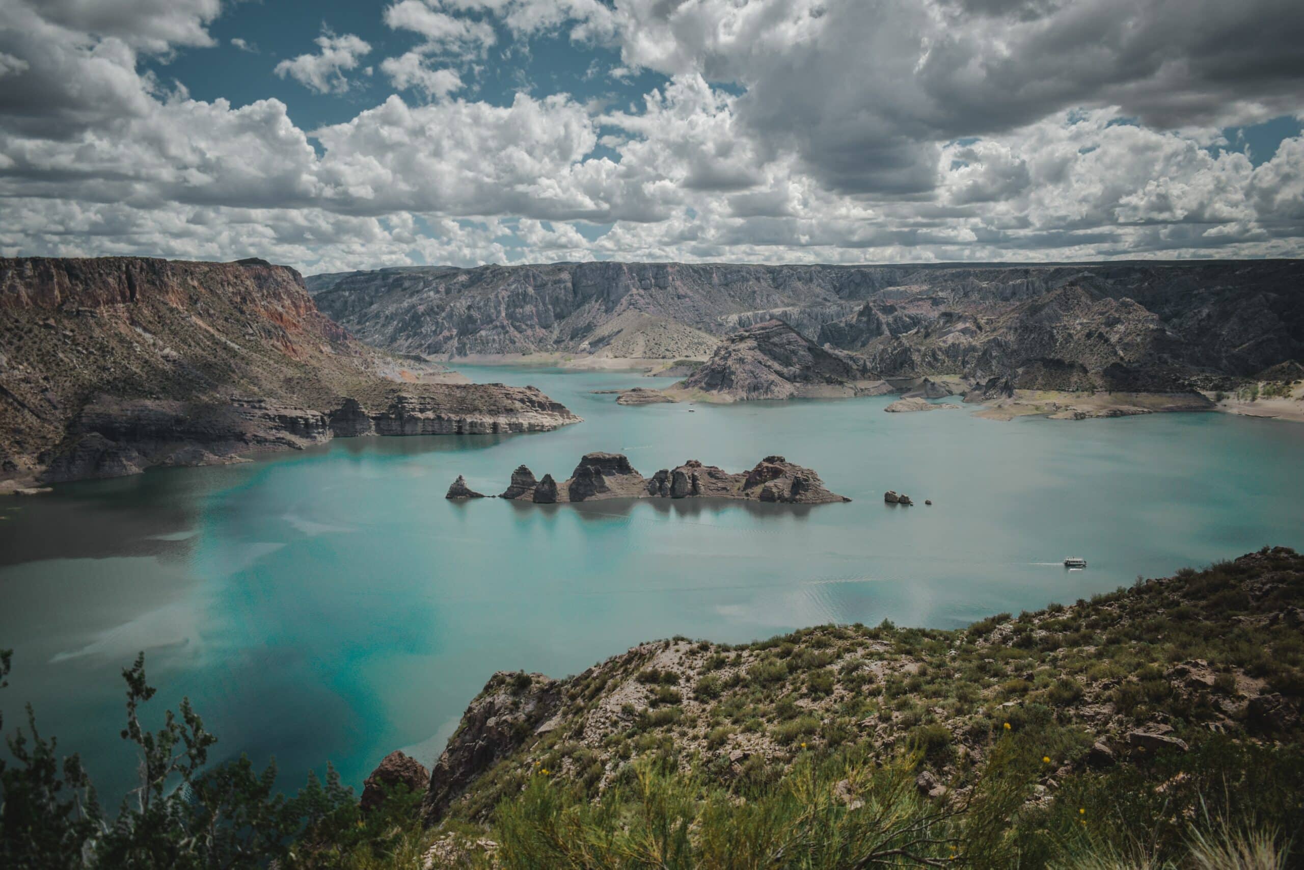Vista de cima do Portal Del Atuel, San Rafael, Mendoza, com um lago em tom azul e rochas no meio da lagoa.