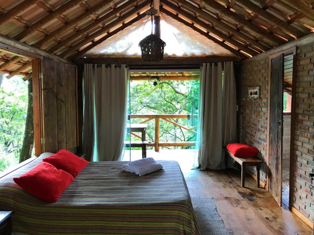 quarto do Chalé Rústico 2 - Retiro Andaluz com cama de casal grande, mas baixa, com mesa, cadeiras de madeira, com varanda e sacada com vista para a natureza