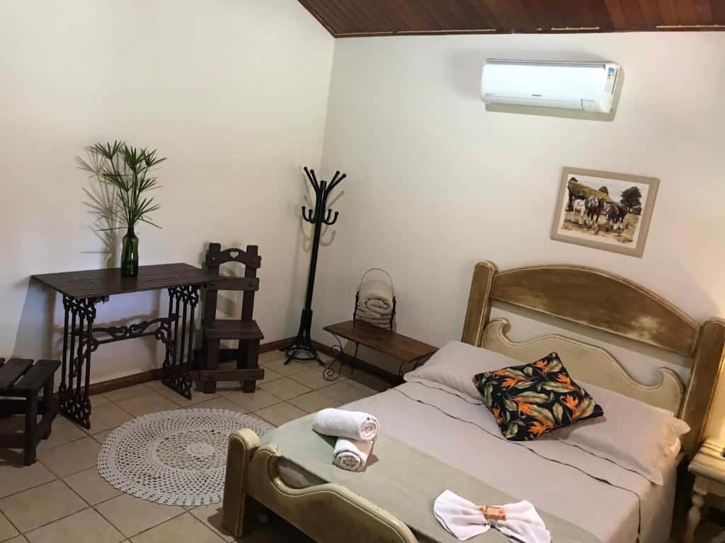 quarto simples com móveis de madeira da Estância das Angolas - Inhotim, com cama de casal, ar-condicionado, mancebo, mesa e cadeira com mesinha de cabaceira