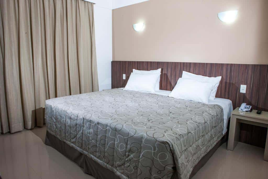 cama de casal bem grande com colcha cinza do Hotel Abba Uno em um quarto amplo com janela grande e cortinas e mesinha de cabeceira com interruptores de ambos os lados