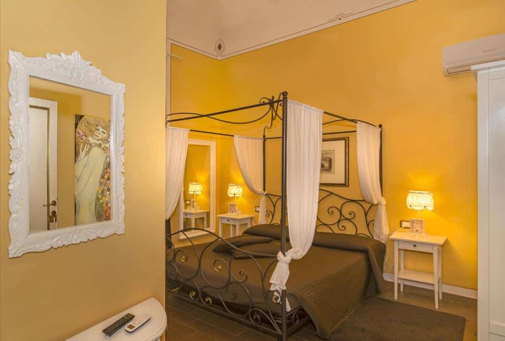 quarto com dossel e cama de casal com detalhes amadeirados e decoração clássica com mesa de cabeceira com luminárias de ambos os lados no Hotel Pisa Tower