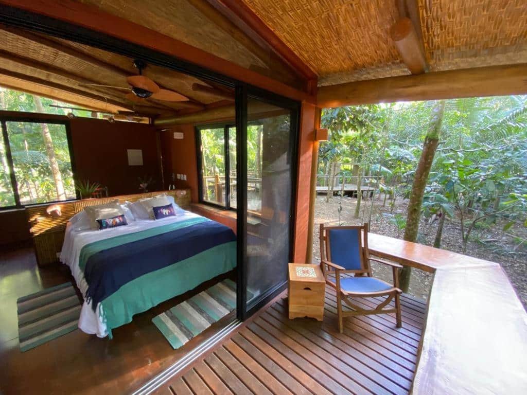 Quarto no  Banana Bamboo Ecolodge com varanda térrea virada para a natureza, uma cama de casal, tudo em madeira e com janelas de vidro, para representar resorts em Ubatuba