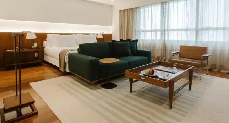 Quarto do Hotel Fasano Belo Horizonte com cama de casal, sofá em frente a cama e mesa de centro e poltrona do lado esquerdo. Representa hotéis em Belo Horizonte