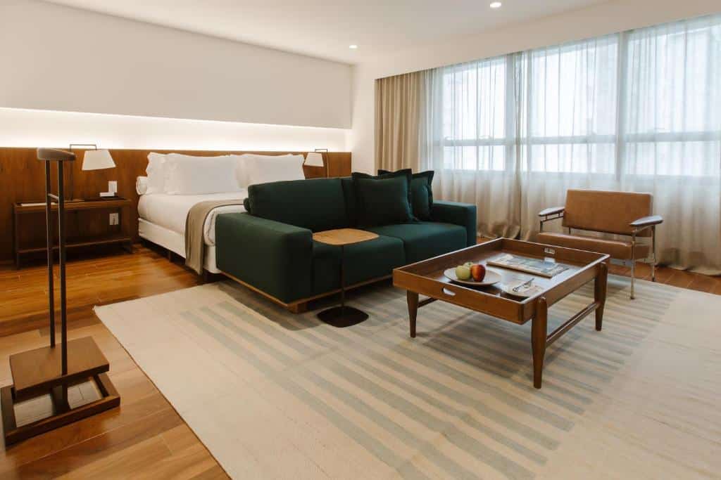 Quarto do Hotel Fasano Belo Horizonte com cama de casal, sofá em frente a cama e mesa de centro e poltrona do lado esquerdo. Representa hotéis em Belo Horizonte