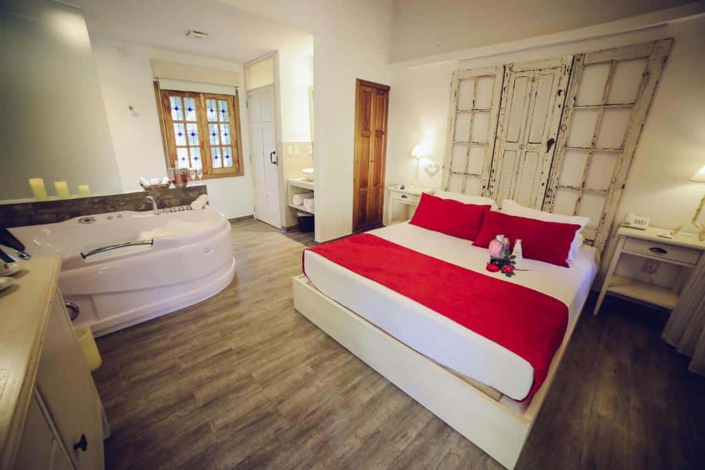 Quarto do Villa Toscana Boutique Hotel - Adults Only com cama de casal, duas comodas ao lado da cama com luminárias, banheira de hidromassagem do lado esquerdo do quarto.