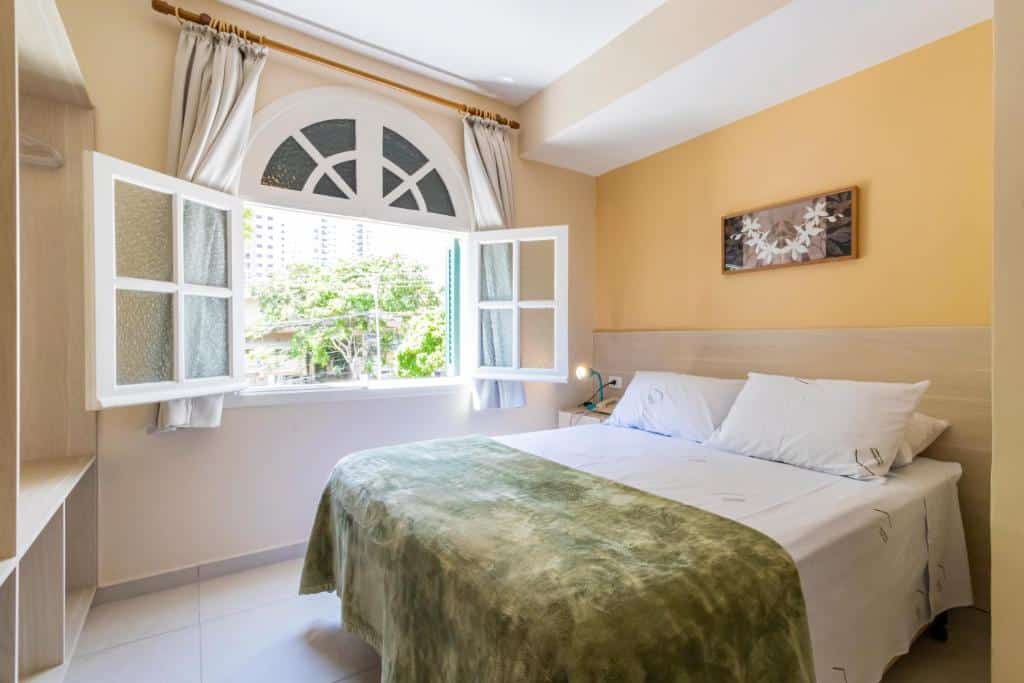Quarto da Hospedaria Santo André com uma cama de casal, uma janela ampla com cortinas e um armário de conceito aberto. Esse é um dos hotéis perto do Allianz Parque.