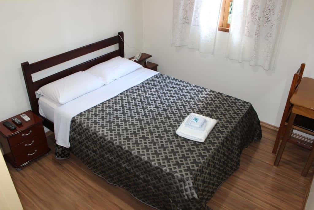 Quarto do Hotel Turiassú com uma cama de casal, chão de madeira, uma janela com cortinas e uma pequena mesa com uma cadeira