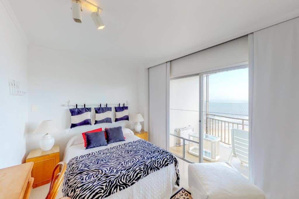 Quarto do Oceana Suites Opus Alpha Apartment com cama de casal, duas cômodas ao lado, mesa de trabalho do lado direito e portas de vidro lado esquerdo com sacada.