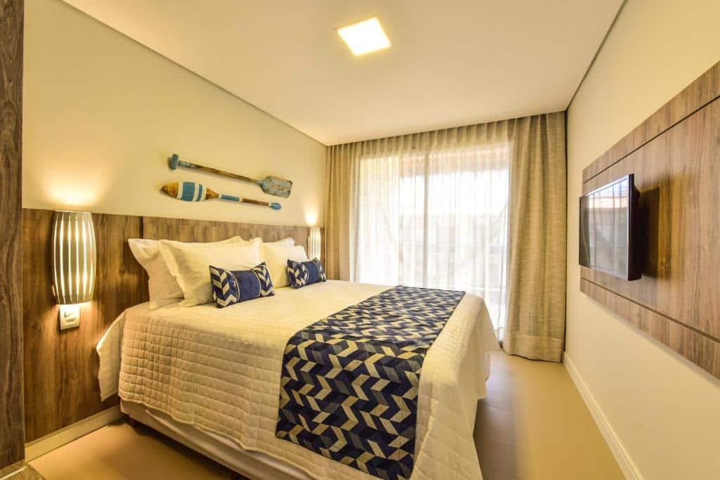 Quarto do Porto das Dunas Praia Hotel com cama de casal, TV em frente a cama, portas de vidro com cortinas brancas que dá acesso a varanda.