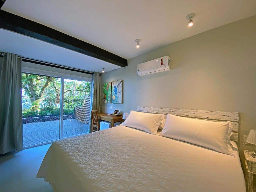 Quarto no Porto Pacuíba Hotel com uma cama de casal grande, um ar-condicionado, uma varanda ampla, uma mesinha de escritório com uma cadeira, e um frigobar
