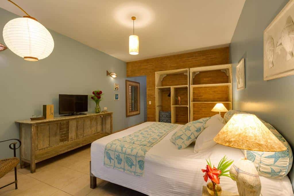 Quarto no Itamambuca Eco Resort com uma cama de casal, um armário de conceito aberto, duas luminárias rústicos no teto, um móvel também rústico em estilo de cômoda com uma televisão em cima