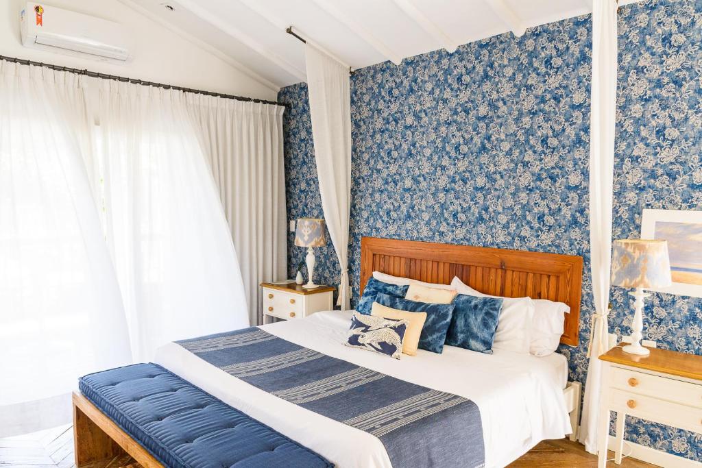Quarto do TW Guaimbê Exclusive Suítes com tudo decorado em azul e branco, uma cama de madeira, uma varanda com cortinas brancas, duas mesinhas de cabeceira, para representar resorts em Ilhabela