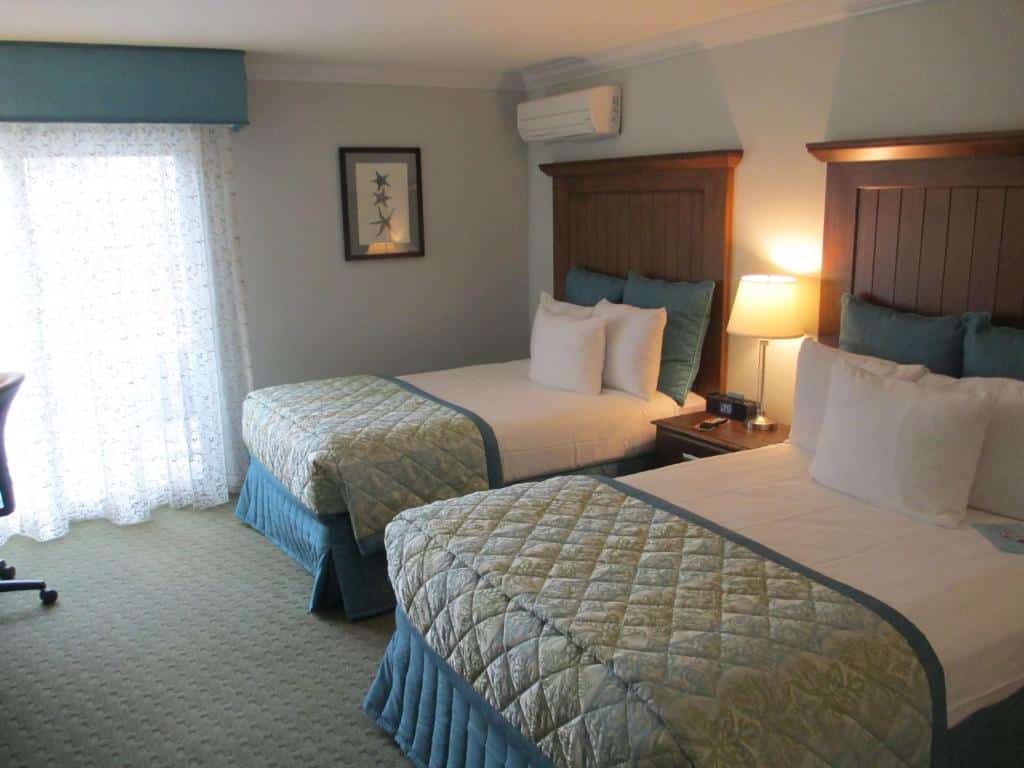 Quarto do Best Western Premier Hotel Del Ma com duas cama de solteiro com uma cômoda ao meio com luminária e janela do lado esquerdo com cortina branca.