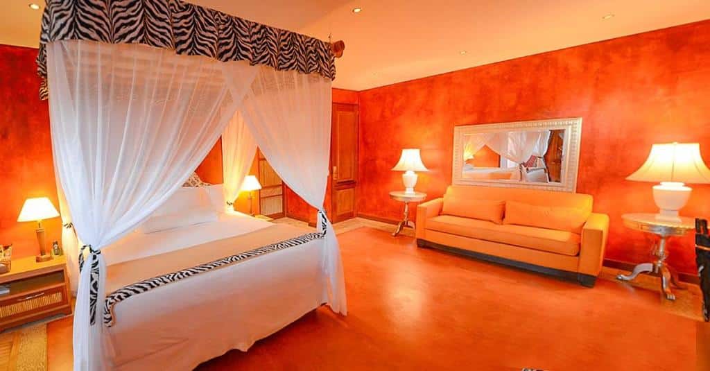 Quarto no DPNY Beach Hotel & SPA com uma cama de casal, um sofá, dois abajures, um espelho e um piso de madeira, para representar resorts em Ilhabela