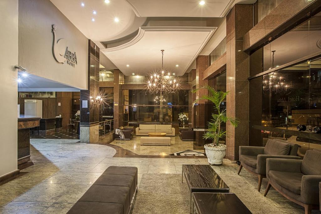 recepção em tons de marrom e com muitas luzes do Abba Hotel, em Betim, com sofás, lustre, mesinhas baixas e o balcão