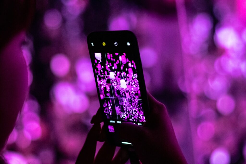 Uma mulher branca segurando um celular na vertical para fotografar diversas luzes roxas