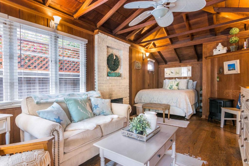 Vista da sala e quarto do Redwood Hollow Cottages com sofá de três lugares cor branca com almofadas do lado esquerdo em frente a janela, com mesa de centro. Ao fundo uma cama de casal com lareira ao lado esquero.