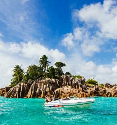 Barco branco no mar perto de pedras e palmeiras verdes durante o dia, ilustrando post seguro viagem Seychelles
